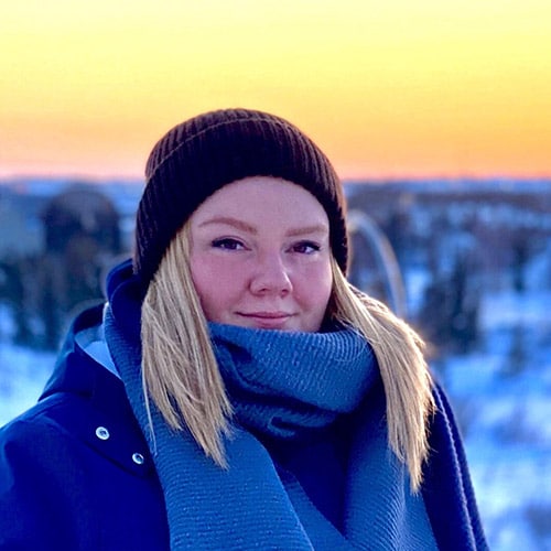 Head shot of Samantha Gruber, outdoors in winter time with colorful sunset in the background.
